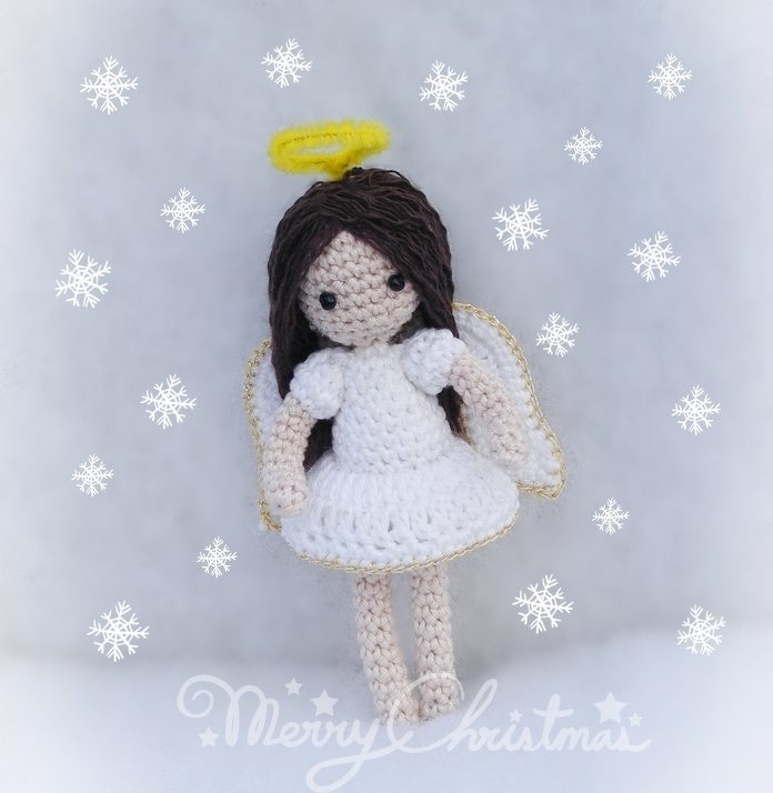 Gehäkelter Amigurumi-Engel mit weißem Kleid, braunen Haaren, gelbem Heiligenschein und goldumrandeten Flügeln vor Schneeflocken-Hintergrund