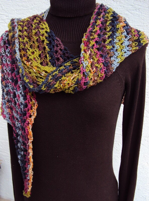 Mehrfarbiger gehäkelter Schal mit offenem Muster, über einem dunkelbraunen Rollkragenpullover drapiert.