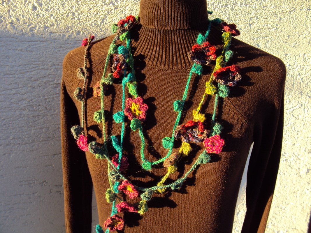 Mehrsträngige, handgehäkelte Kette mit bunten Blüten und grünen Blättern auf dunkelbraunem Pullover