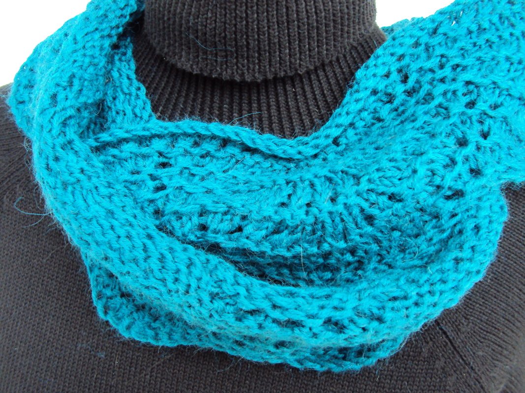 Türkiser gestrickter Loop mit offenem Maschenmuster auf schwarzem Rollkragen