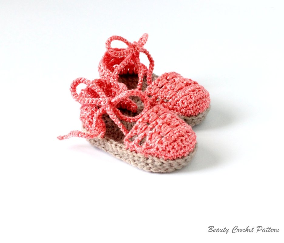 Coral pink and beige crocheted baby sandals with tie straps on a white background.