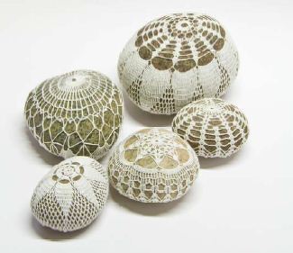 Verschiedene Steine mit weißen gehäkelten Überzügen in mehreren Mustern auf hellem Grund