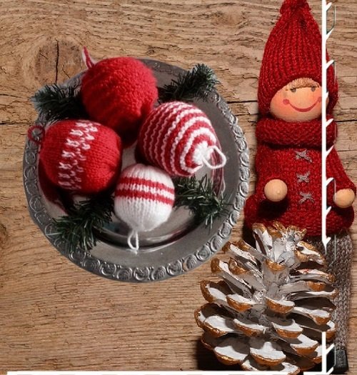 Gestrickte rote und weiß gestreifte Weihnachtskugeln auf silbernem Teller mit Tannengrün; roter Strickwichtel und gold-weiß bemalter Zapfen auf Holzuntergrund.