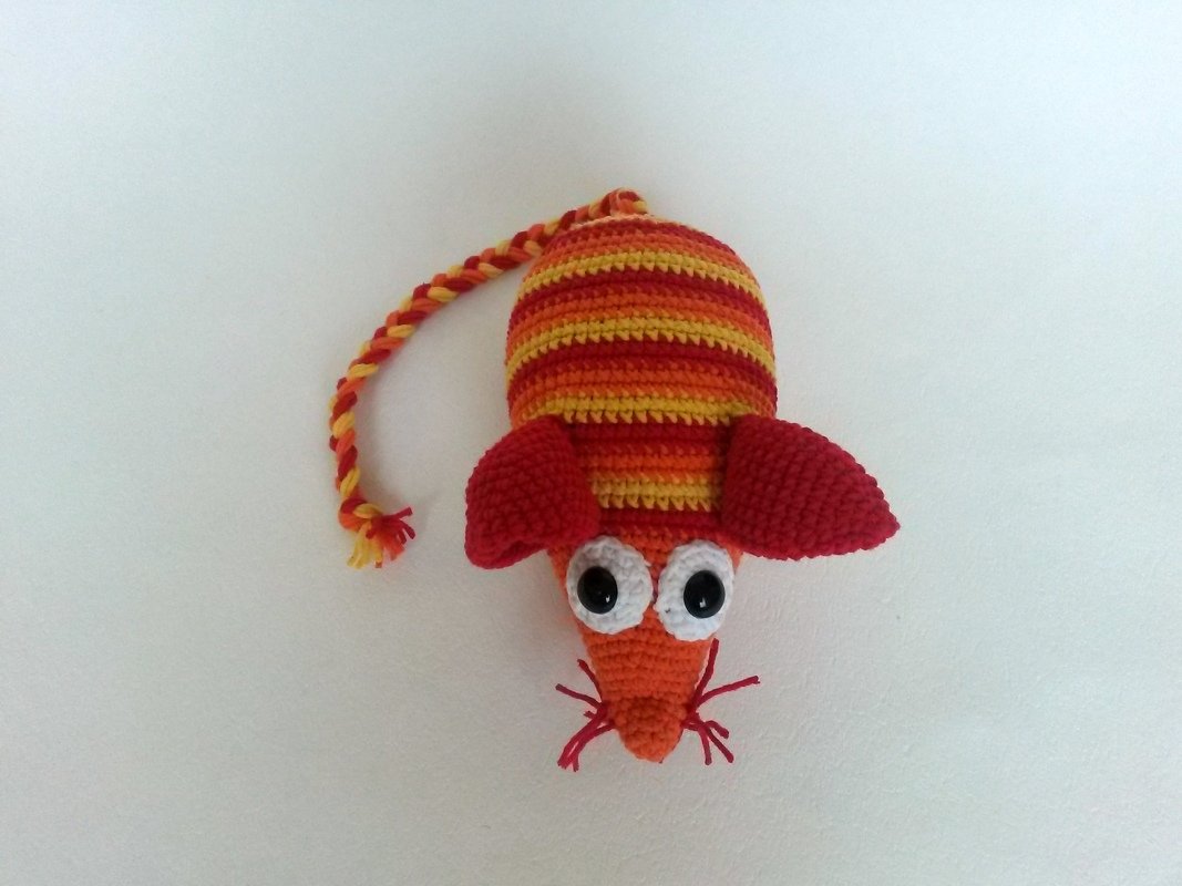 Gehäkelte Amigurumi-Maus gestreift in Orange und Gelb mit roten Ohren und geflochtenem Schwanz auf hellem Hintergrund