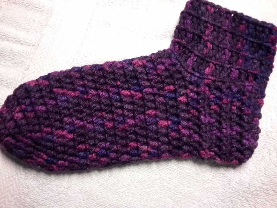 Gehäkelte Socke in melierten Lila- und Pinktönen auf weißem Handtuch