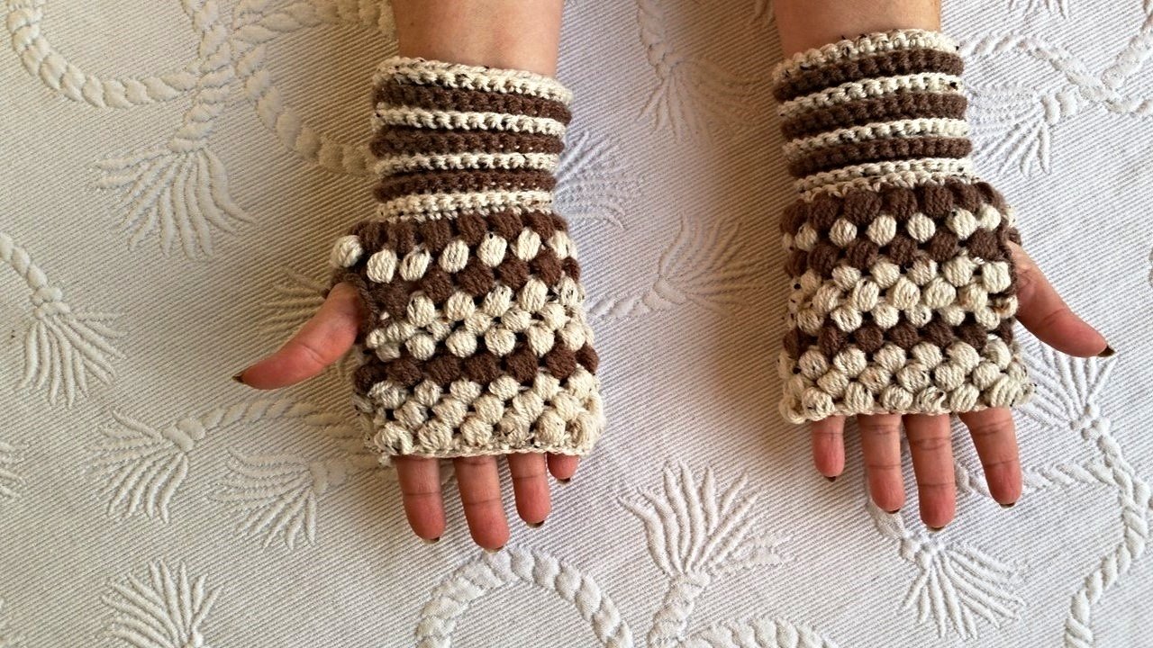 Nahaufnahme von Händen mit gehäkelten, fingerlosen Armstulpen in Braun und Beige mit Noppenmuster