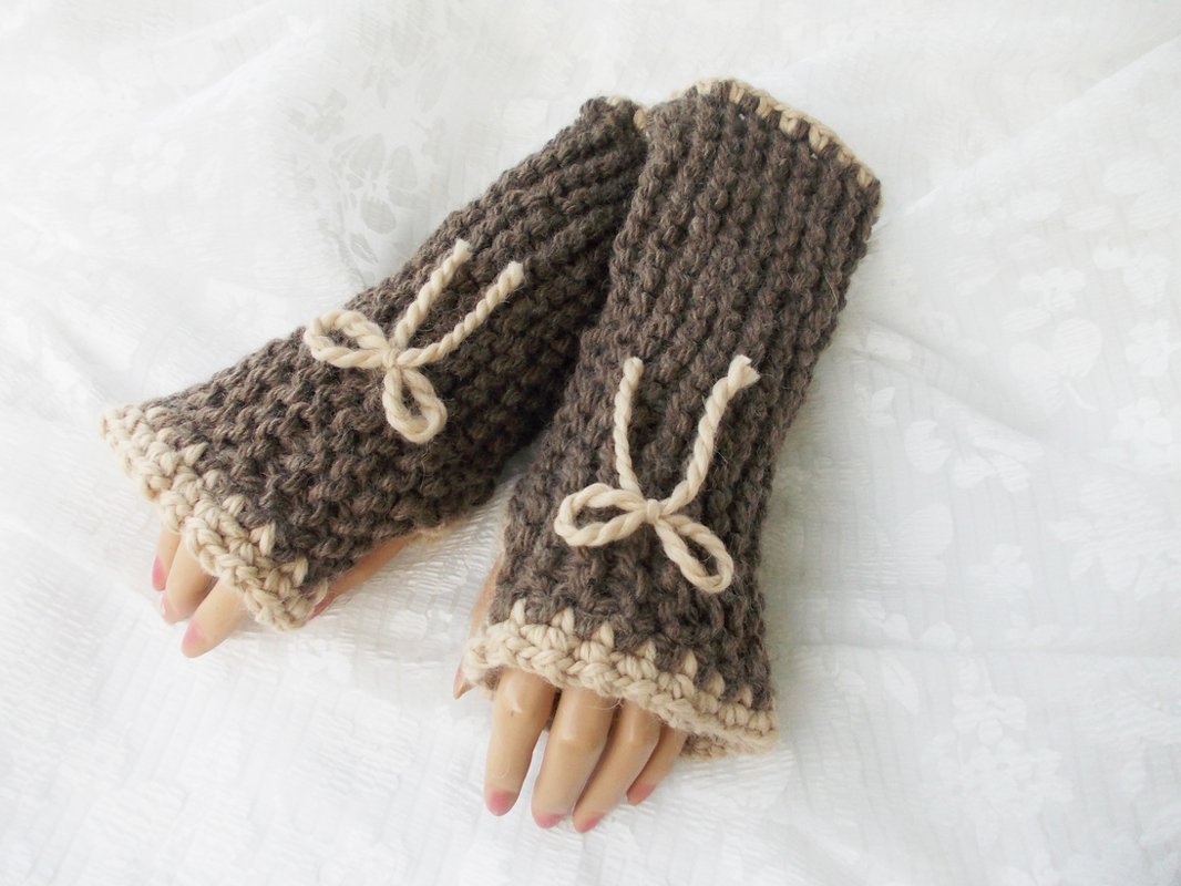 Braune, grob gestrickte fingerlose Armstulpen mit beigen Schleifen und kontrastierendem Bündchen auf hellem Hintergrund