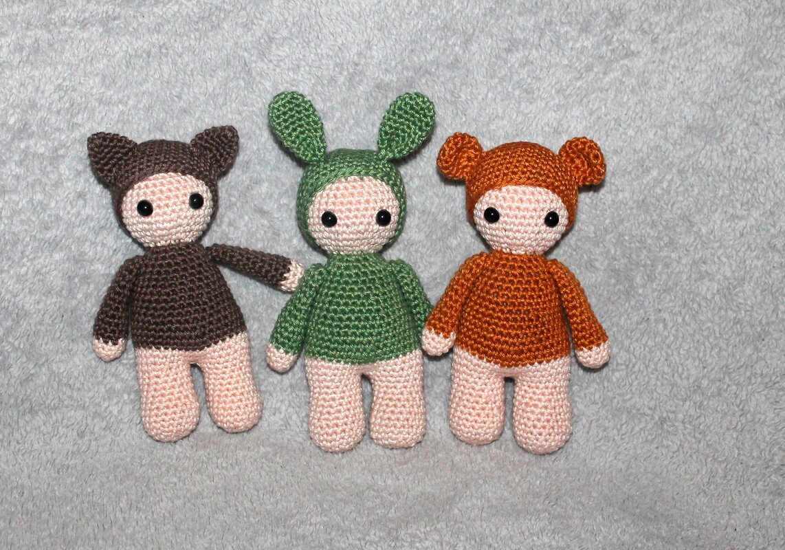 Three crocheted amigurumi dolls with pointy brown, long green, and rounded orange animal ears on a grey background.
