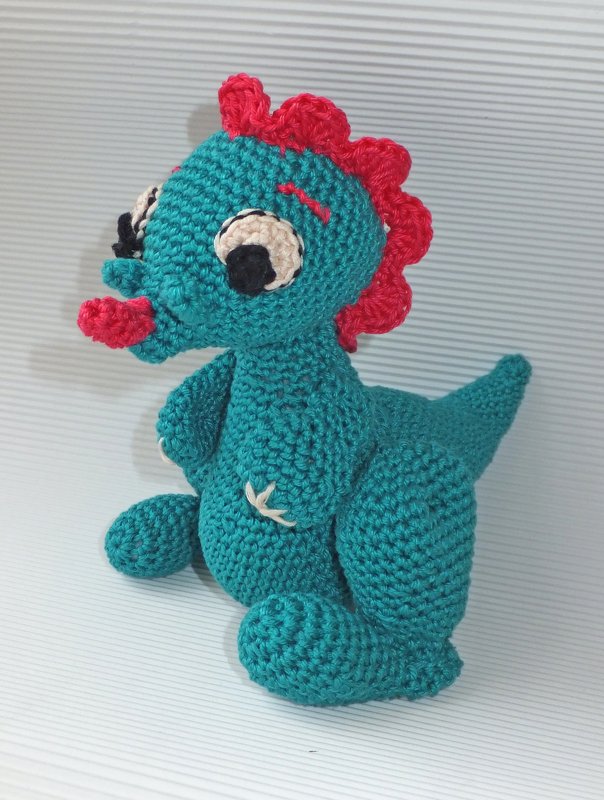 Türkis gehäkelter Amigurumi-Drache mit rotem Kamm und weißen Augen, sitzend