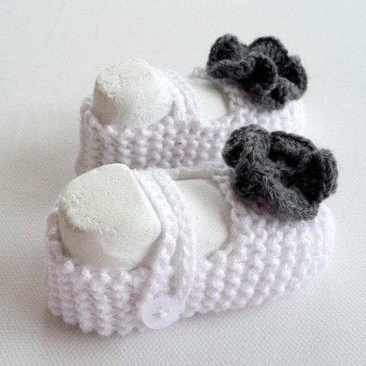 weiße gestrickte Babyschühchen im Ballerina-Stil mit grauer Blüte und Knopfriemen