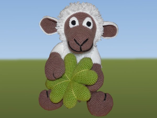 Sitzendes gehäkeltes Amigurumi-Schaf in Braun und Weiß mit großem grünem Kleeblatt