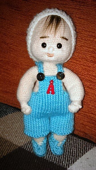 Gehäkelte Amigurumi-Puppe: Babyjunge mit weißem Häubchen, blauer Latzhose und rotem A