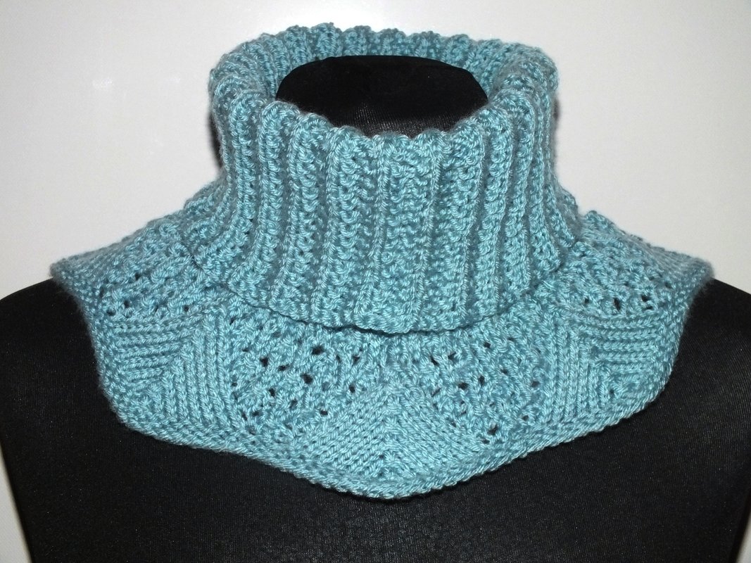 Türkis gestrickter Kragenschal mit hohem Rippenkragen und Lochmuster auf dunkler Büste.