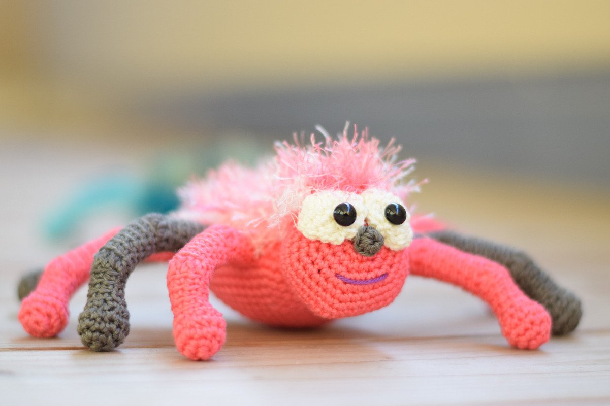 rosa gehäkelte Amigurumi-Spinne mit weißen Augen und grauen Beinen