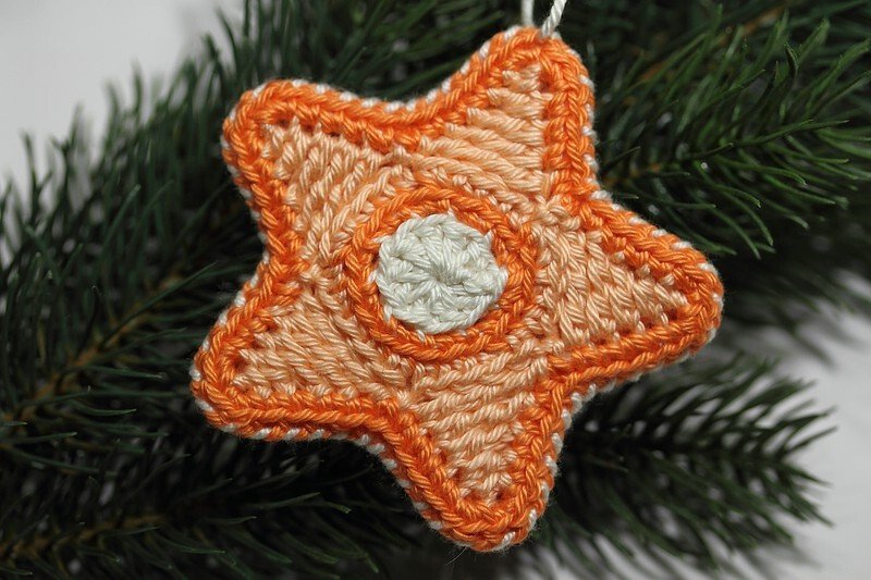 Gehäkelter fünfzackiger Sternanhänger in Orange und Creme an Tannenzweig