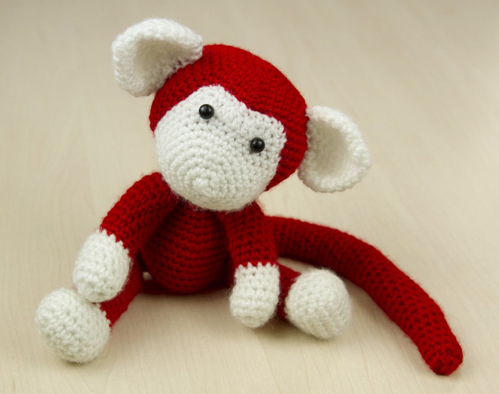 Sitzender gehäkelter Amigurumi-Affe, rot mit weißen Ohren, Schnauze und Pfoten.