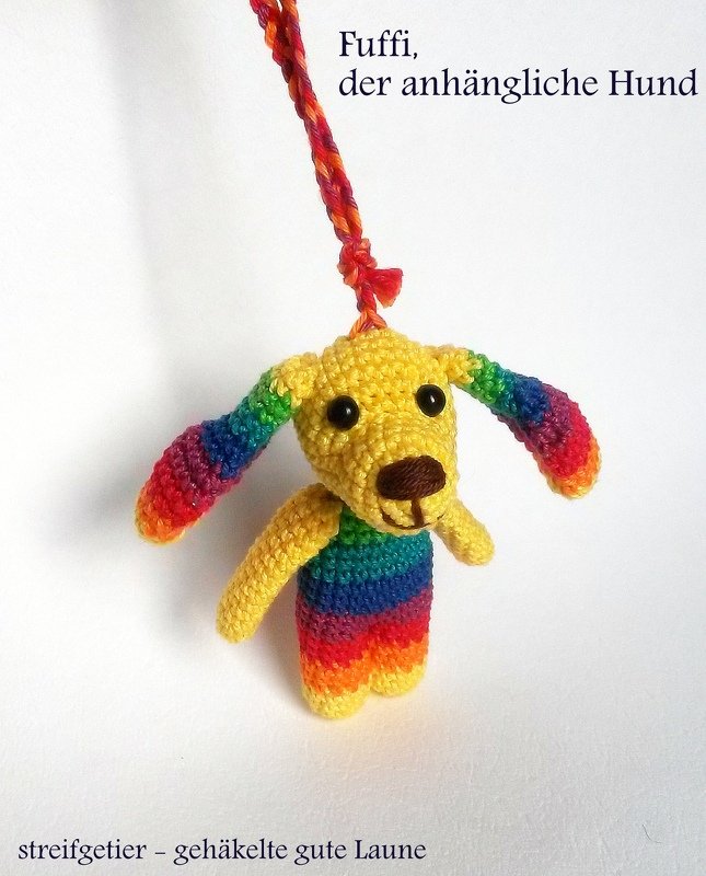 Gehäkelter Amigurumi-Hund mit gelbem Kopf und regenbogenfarbenem Körper an bunter Kordel