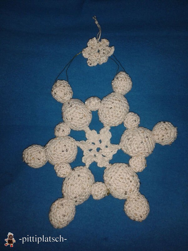 Gehäkelter sternförmiger Anhänger aus cremeweißem Garn mit Pailletten vor blauem Hintergrund