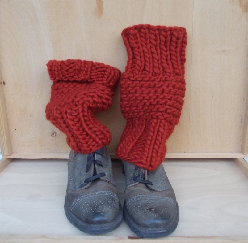 Rote grob gestrickte Beinstulpen über dunklen Leder-Ankle-Boots