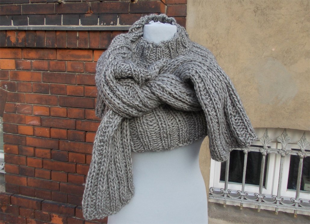 Grauer grob gestrickter Pullover mit voluminösem, vorne geknotetem Schalkragen auf einer Schaufensterpuppe.