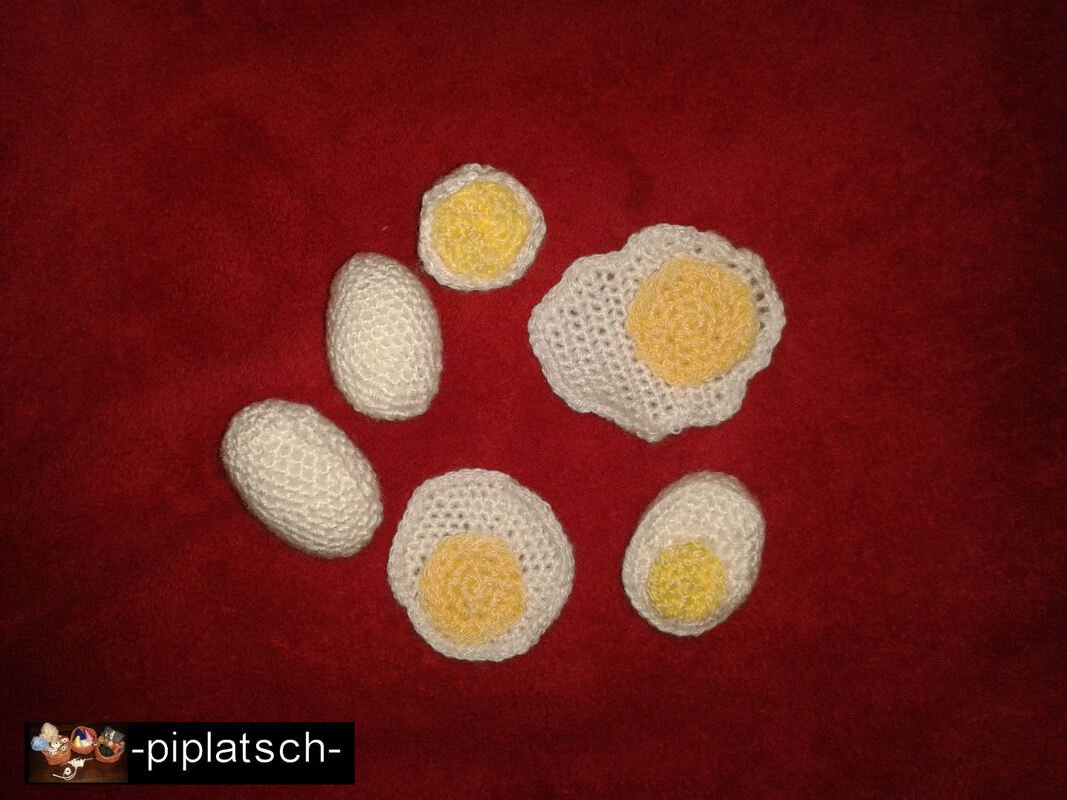Gehäkelte weiße und gelbe Spiel-Eier und Spiegelei auf rotem Stoff