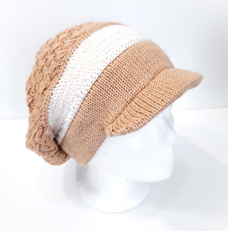 Beige gestrickte Schirmmütze mit weißem Streifen und Zopfmuster auf weißem Schaufensterkopf
