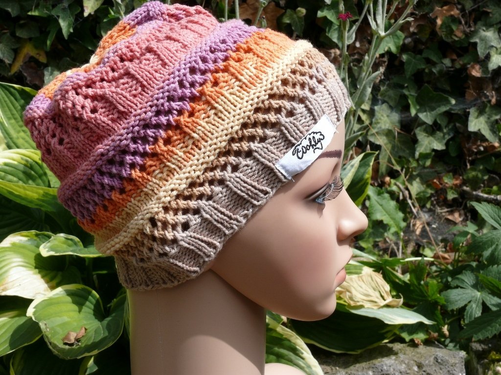 Gestrickte Damenmütze in Pastellstreifen mit Ajourmuster auf Schaufensterpuppe vor Grünpflanzen