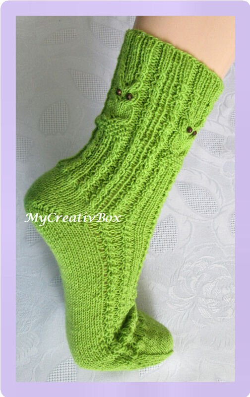 Grüne gestrickte Kindersocke mit Zopfmuster und Eulenapplikationen, an einem Bein getragen.