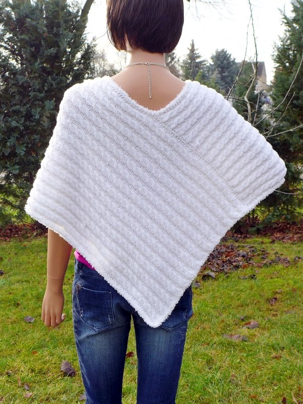 Rückenansicht einer Person mit weißem gestricktem Poncho mit diagonalem Zopfmuster, kombiniert zu Jeans