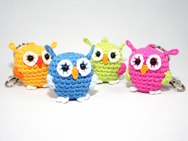 Four colorful crocheted amigurumi owl keychains in blue, pink, green and orange on a white background