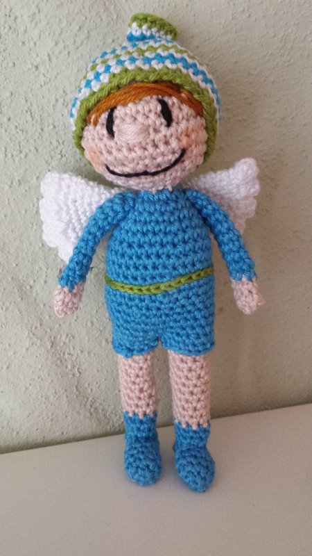 Gehkelter Amigurumi-Engel frontal mit blauem Outfit, weien Flgeln, gestreifter Mtze und freundlichem Lcheln