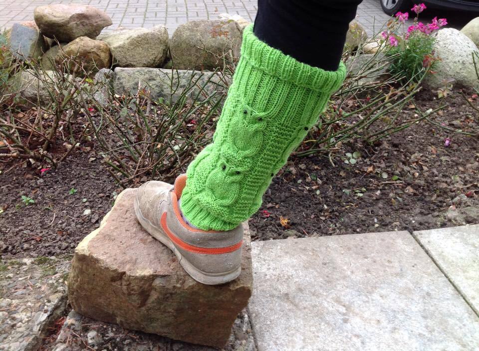 Grüne, gestrickte Beinstulpe mit Eulenmotiv an einem Bein über dunkler Hose