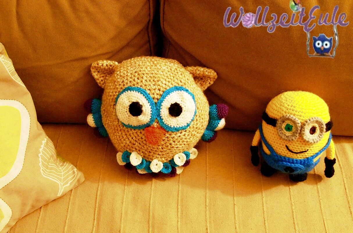 Rundes handgehäkeltes Eulen-Kissen mit blauen Augenringen und kleiner gelber Häkelfigur auf einem senfgelben Sofa
