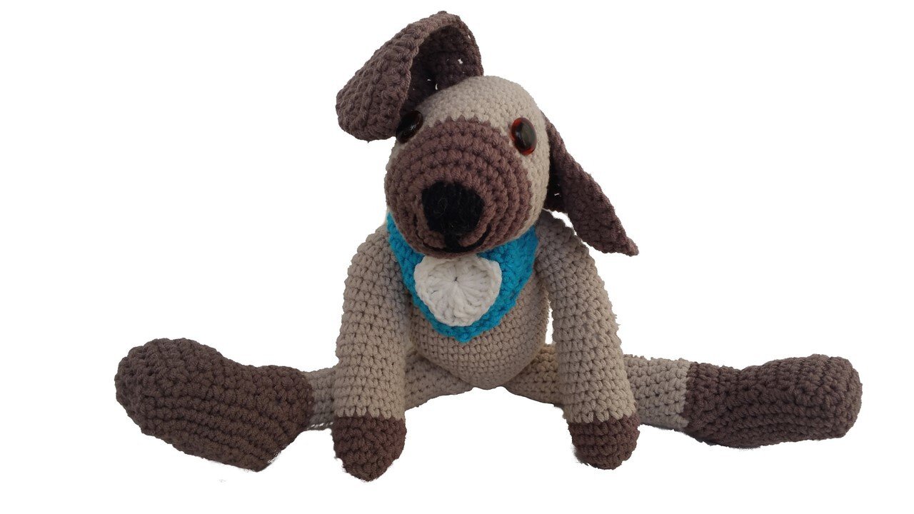 Gehäkelter Amigurumi-Hund in Beige und Braun mit blauem Halstuch und weißem Herz