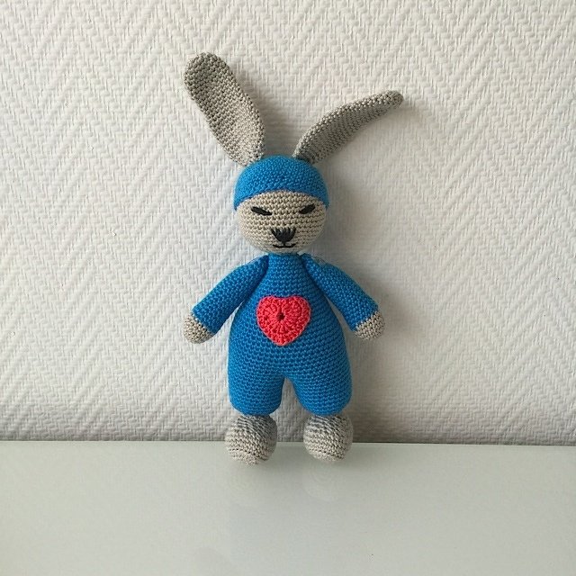 Gehäkelter Amigurumi-Hase in Grau mit langen Ohren, blauem Anzug und rotem Herz auf dem Bauch
