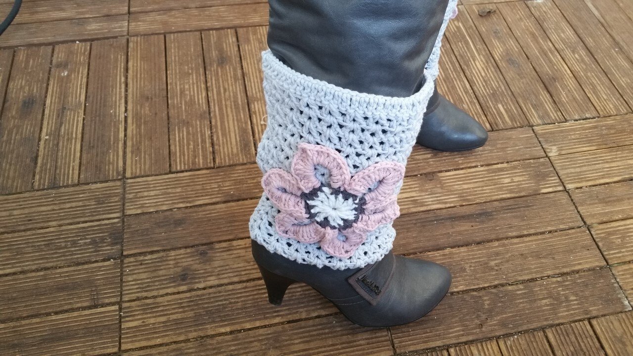 Hellgraue gehäkelte Beinstulpen mit rosa Blüte an dunklen Stiefeletten