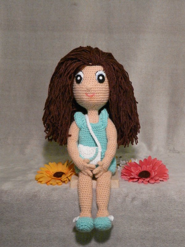 Gehäkelte Amigurumi-Puppe mit braunen Garnhaaren, türkisfarbenem Kleid und weißer Umhängetasche, sitzend