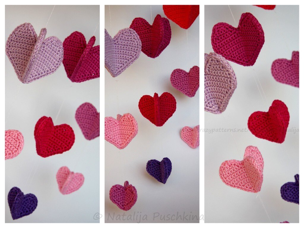 Handgehäkelte Herzen in Rosa, Rot und Lila als Girlande aufgehängt.