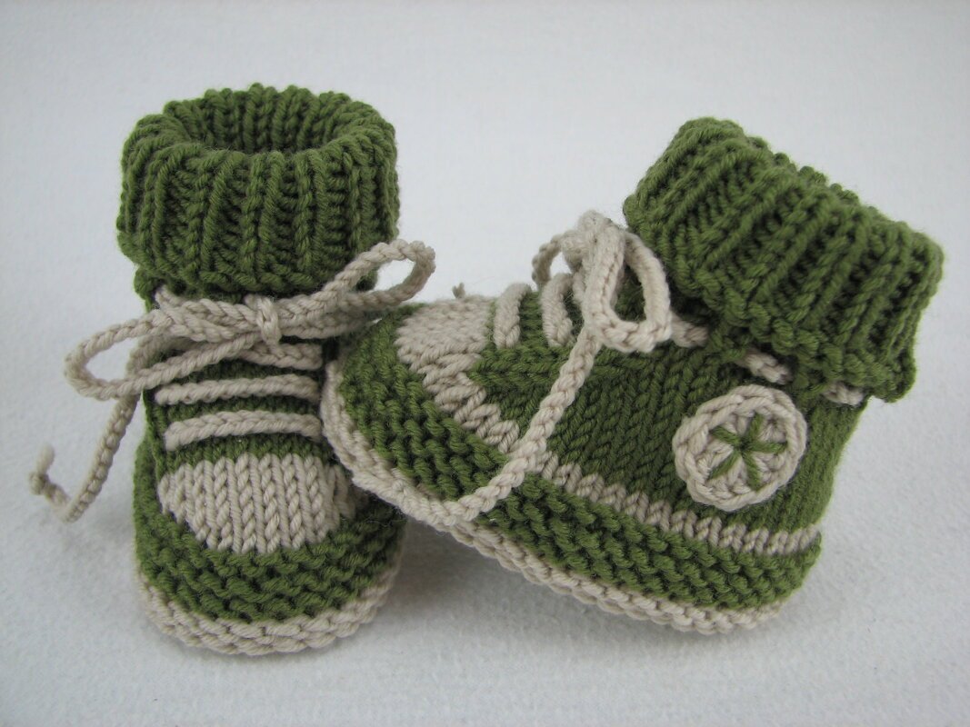 Pair of green and beige knitted baby booties with folded rib cuffs, laces and star detail