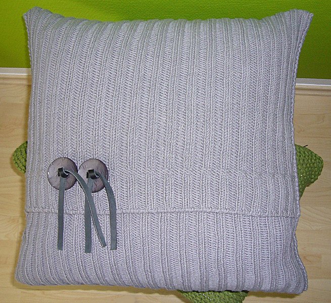 Hellgraues Strickkissen mit vertikalem Rippenmuster und zwei Holzknöpfen mit grauen Bändern