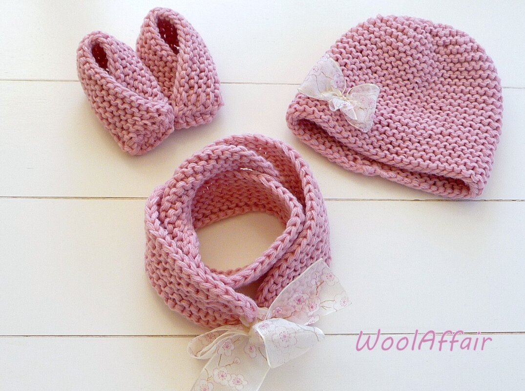 Rosa gestricktes Baby-Set mit Mütze, Babyschühchen und Schlauchschal, mit feinen Schleifen, auf hellem Hintergrund