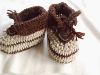 Zwei gehäkelte Babyschuhe mit braunen und beigen Streifen auf hellem Hintergrund