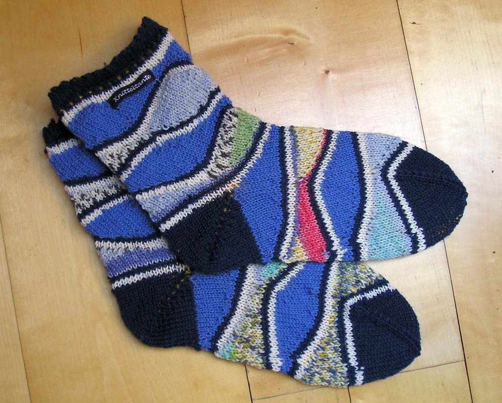 Paar handgestrickter Socken in Blau mit geometrischem Muster auf hellem Holzboden