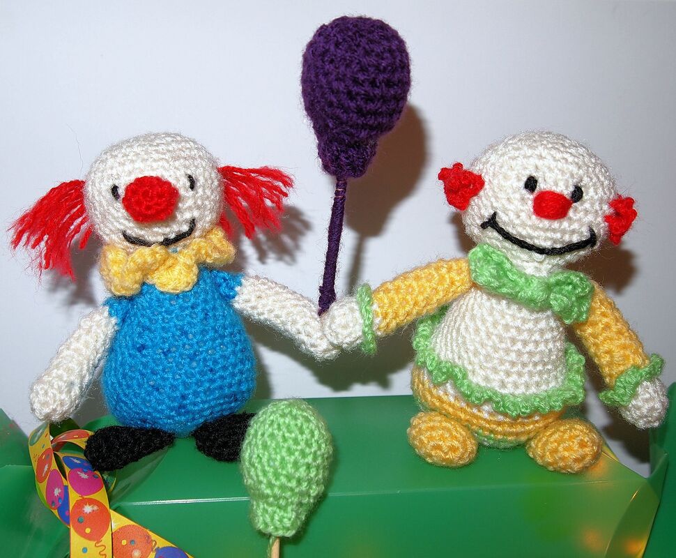 Zwei handgehäkelte Amigurumi-Clowns mit roter Nase und lila Luftballon