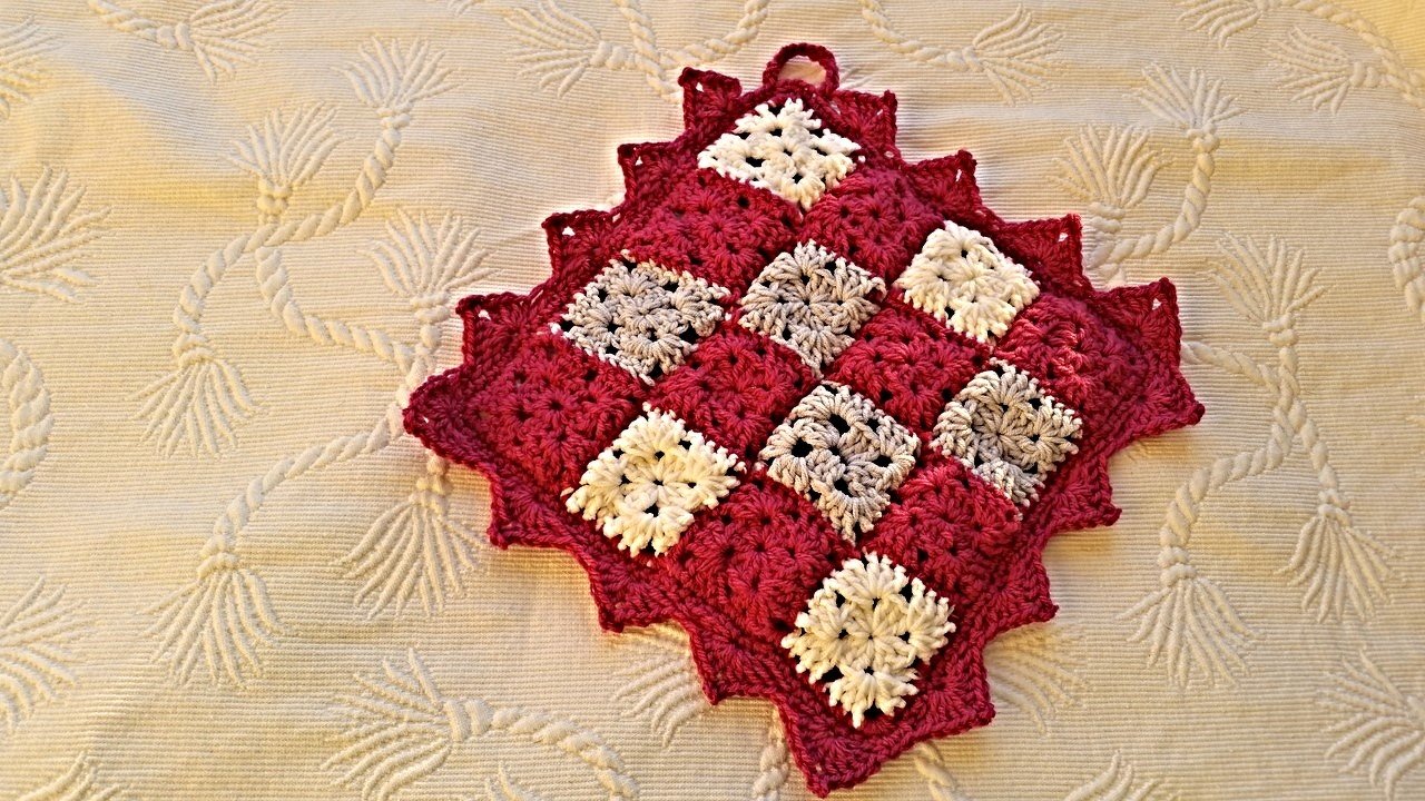 Gehäkelter Topflappen in Zackenform aus Granny-Squares in Rot, Weiß und Grau auf hellem Stoff