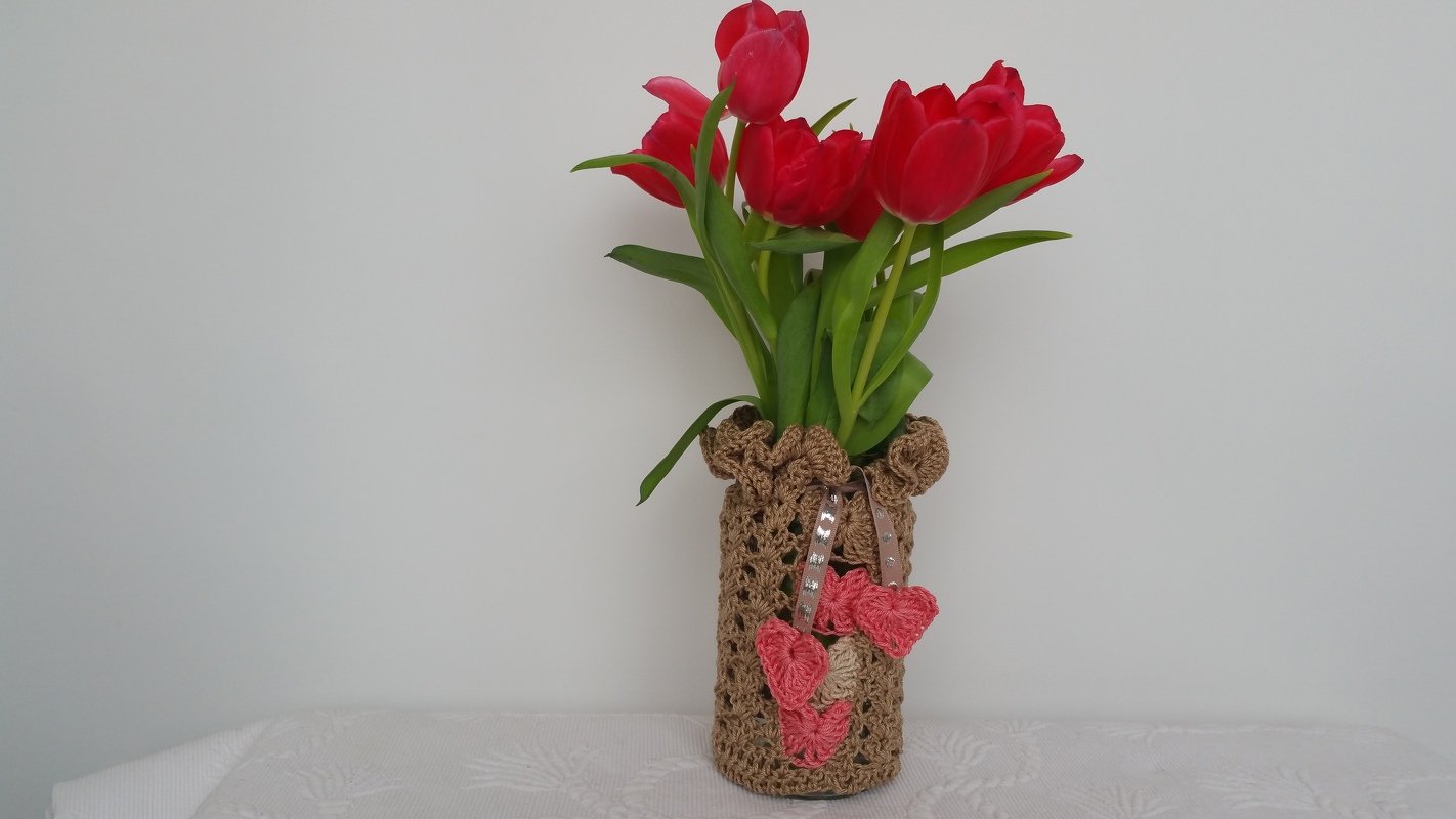 Rote Tulpen in Vase mit braun gehäkelter Hülle und rosafarbenen Herzen am Band