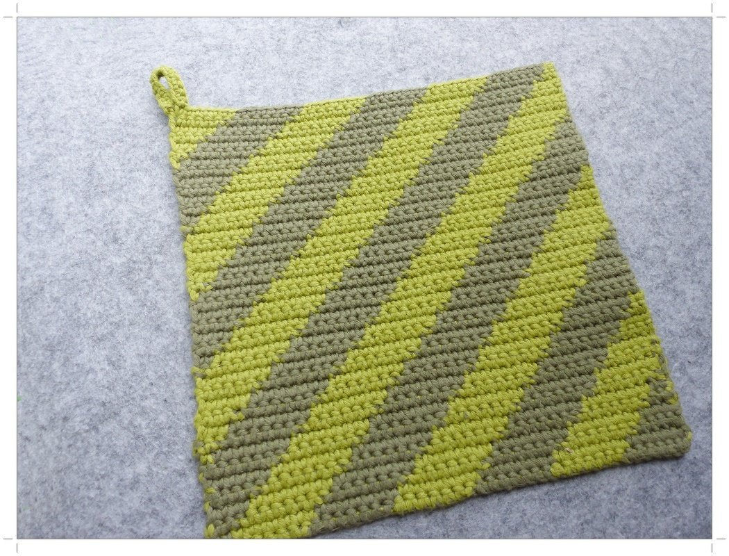 Quadratischer gehäkelter Topflappen mit diagonalen Streifen in Lindgrün und Khaki, mit Aufhängeschlaufe, auf hellem Untergrund.
