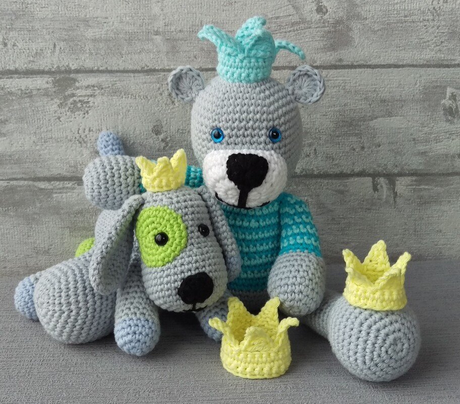 Amigurumi-Set: sitzender grauer Bär mit türkiser Krone, liegender grauer Hund mit gelber Krone und zwei lose gelbe Häkelkrönchen.
