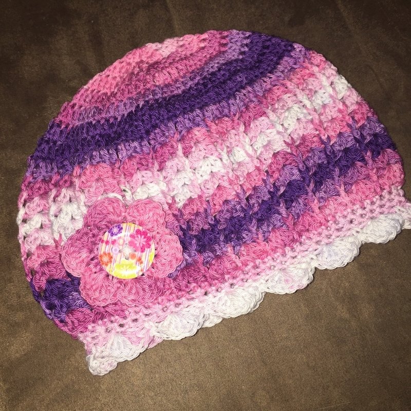 Gehäkelte Babymütze in rosa, lila und weiß mit Häkelblüte und Knopf