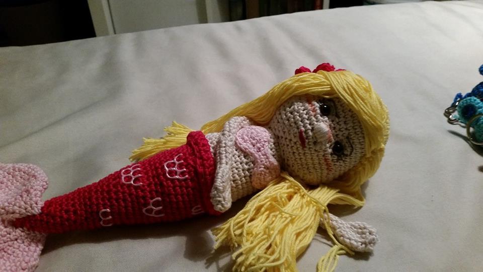 Gehäkelte Meerjungfrau-Amigurumi mit gelbem Haar, rosa Oberteil und rotem Schwanz, liegend auf hellem Untergrund.